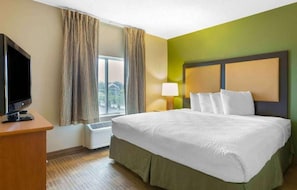 Una habitación de hotel con cama, televisión, ventana con cortinas, lámpara y un calentador de pared.