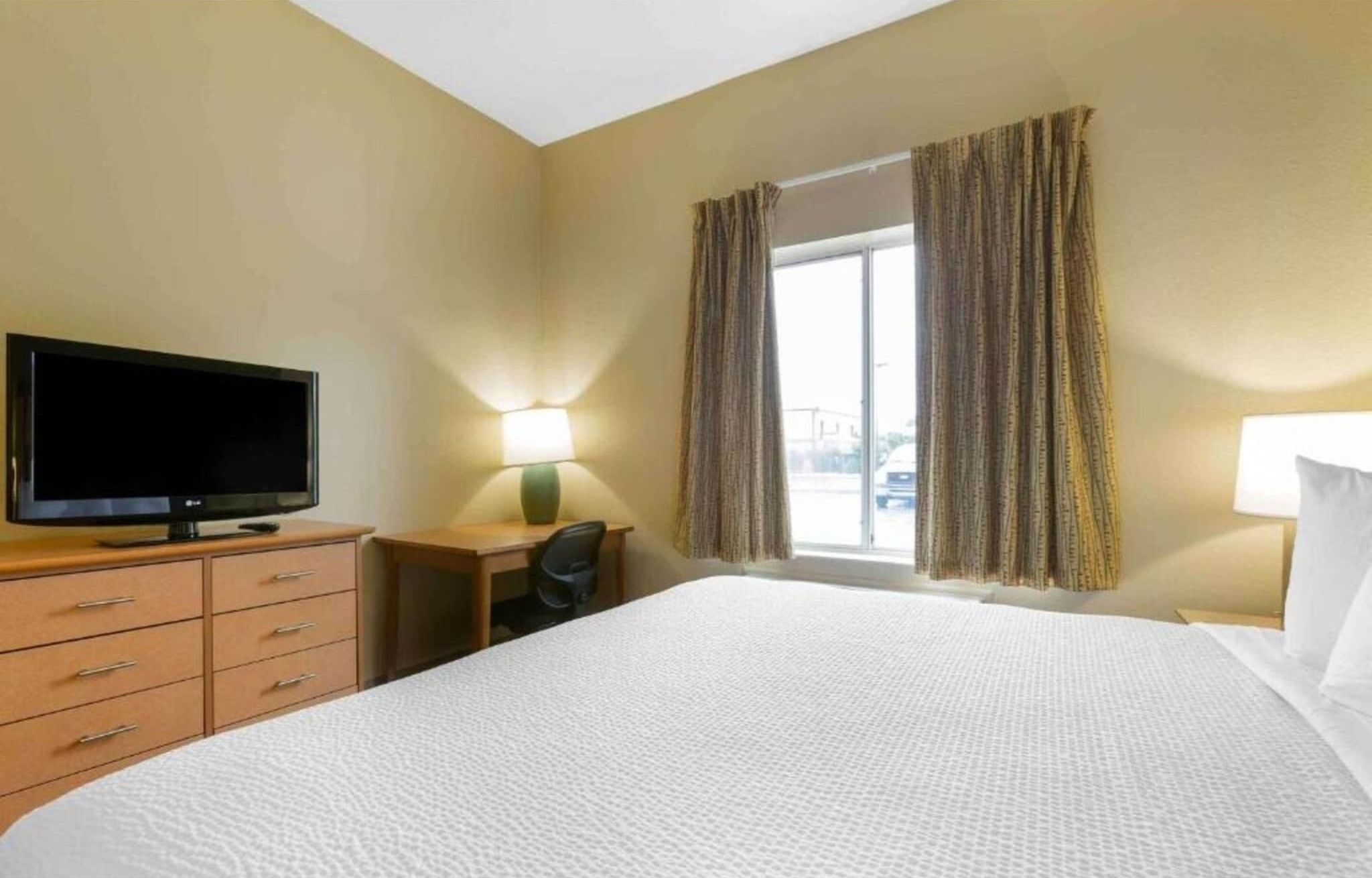 Une chambre d’hôtel avec un lit, une télévision, un bureau et une fenêtre avec des rideaux.
