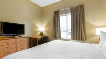 Une chambre d’hôtel avec un lit, une télévision, un bureau et une fenêtre avec des rideaux.