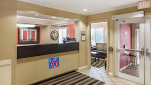 Un vestíbulo de hotel con una recepción, un reloj, una pared roja y una puerta que indica 'EXIT'.