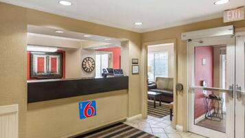 A hotel lobby with a reception desk, a clock, a red wall, and a door marked 'EXIT'.