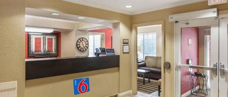A hotel lobby with a reception desk, a clock, a red wall, and a door marked 'EXIT'.