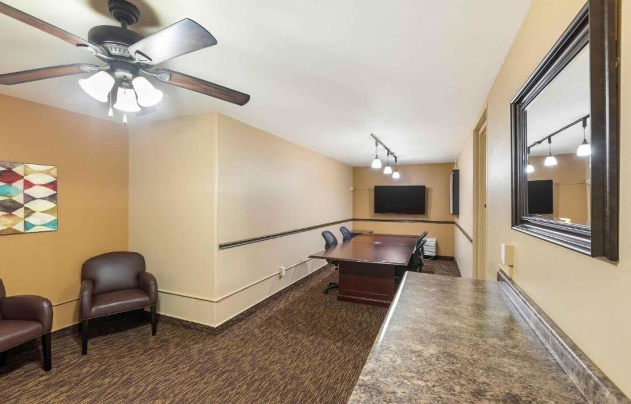 A conference room with a ceiling fan, a long table with chairs, a flat-screen TV, and a large mirror.
