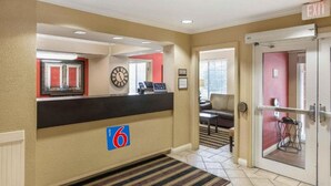 Un vestíbulo de hotel con una recepción, un reloj, una pared roja y una puerta que indica 'EXIT'.
