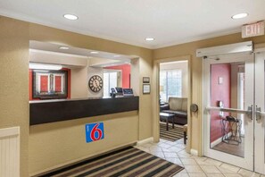 Un vestíbulo de hotel con una recepción, un reloj, una pared roja y una puerta que indica 'EXIT'.