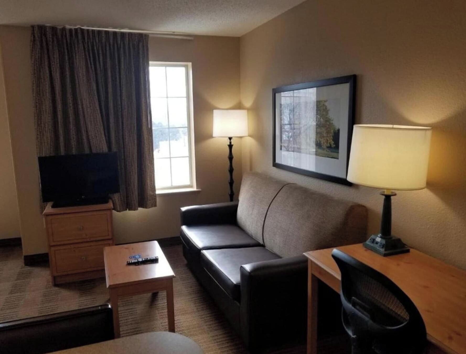 A hotel room with a sofa, a desk, a television, a lamp, and a window with curtains.