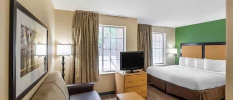 A hotel room with a bed, a television on a wooden dresser, a sofa, and two windows with curtains.