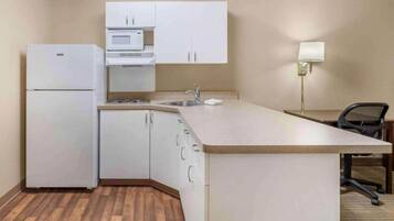 A compact kitchen with a refrigerator, microwave, sink, and a small dining area with a chair.