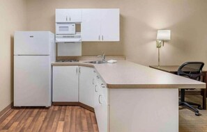 A compact kitchen with a refrigerator, microwave, sink, and a small dining area with a chair.