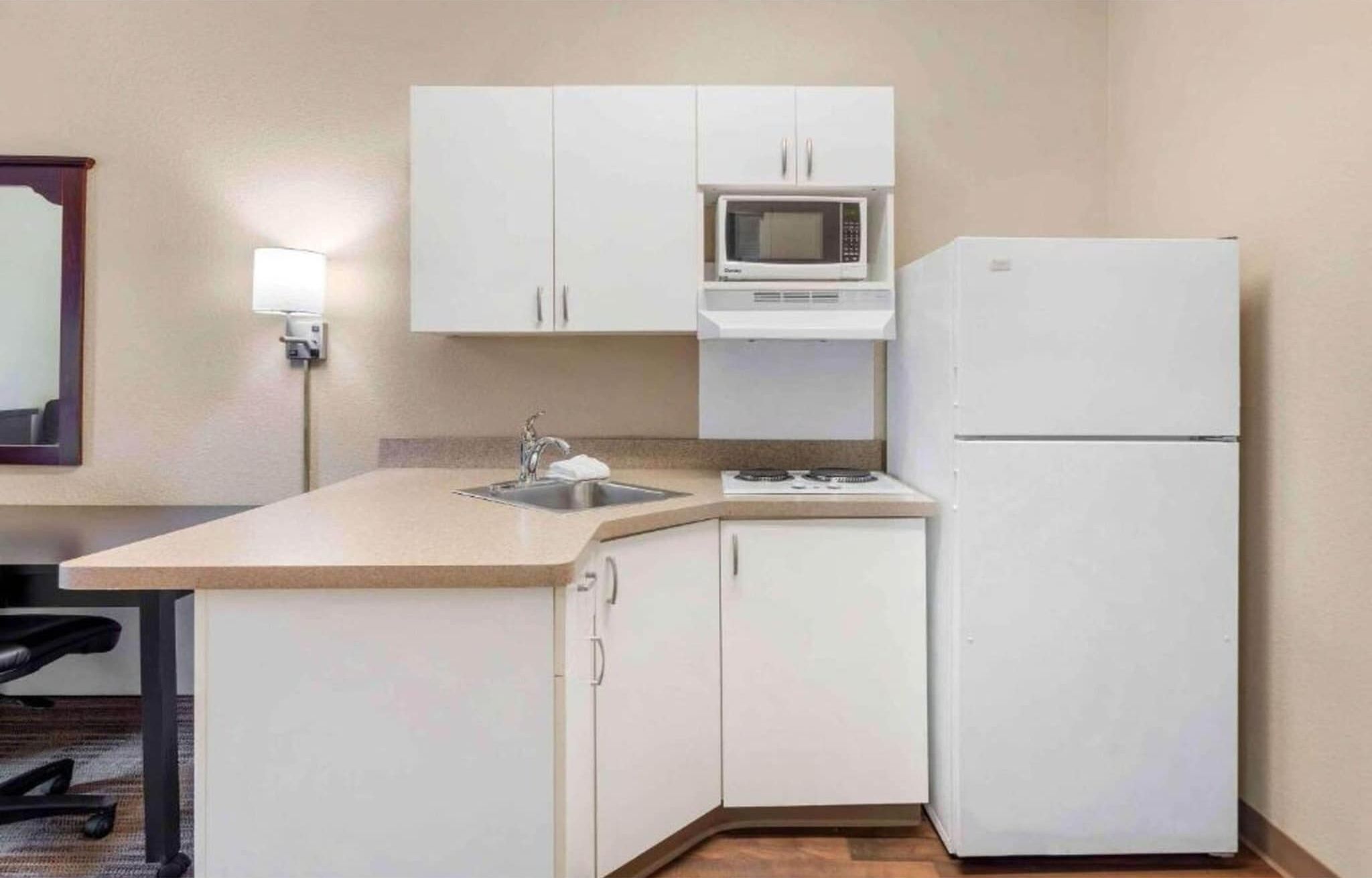 A compact kitchen with white cabinets, a microwave, a refrigerator, and a sink.