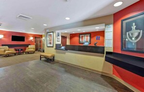 A hotel reception area with a reception desk, seating area, and a television screen.