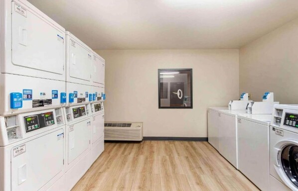 A laundry room with multiple washing machines and dryers, a framed picture on the wall, and a vent on the floor.