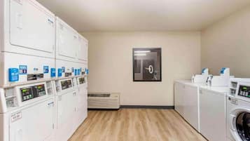 A laundry room with multiple washing machines and dryers, a framed picture on the wall, and a vent on the floor.