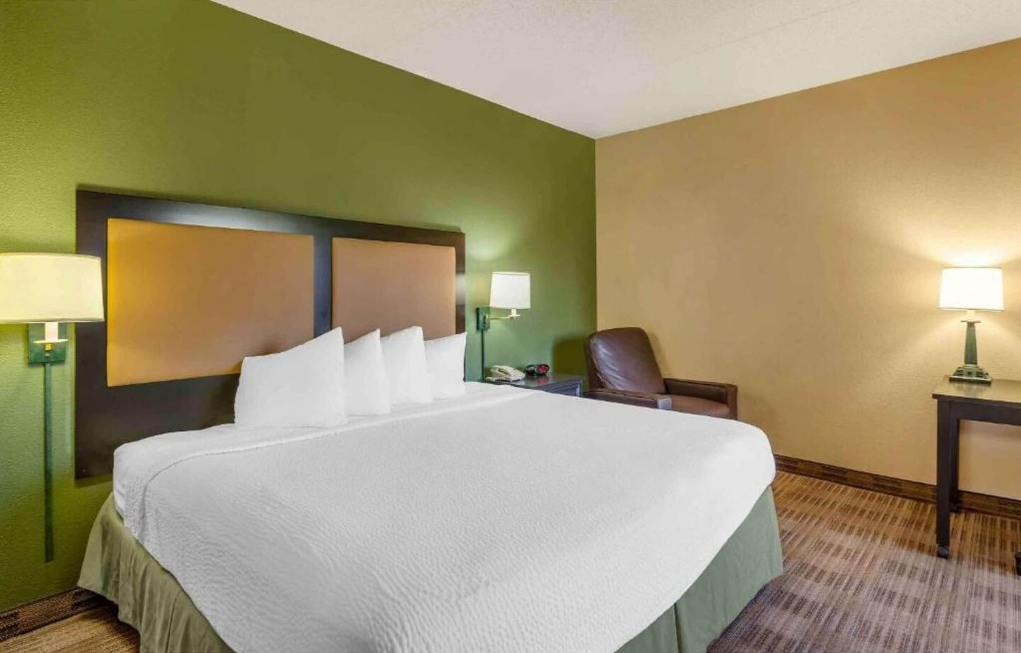 A hotel room with a large bed, two bedside lamps, a chair, and a nightstand.
