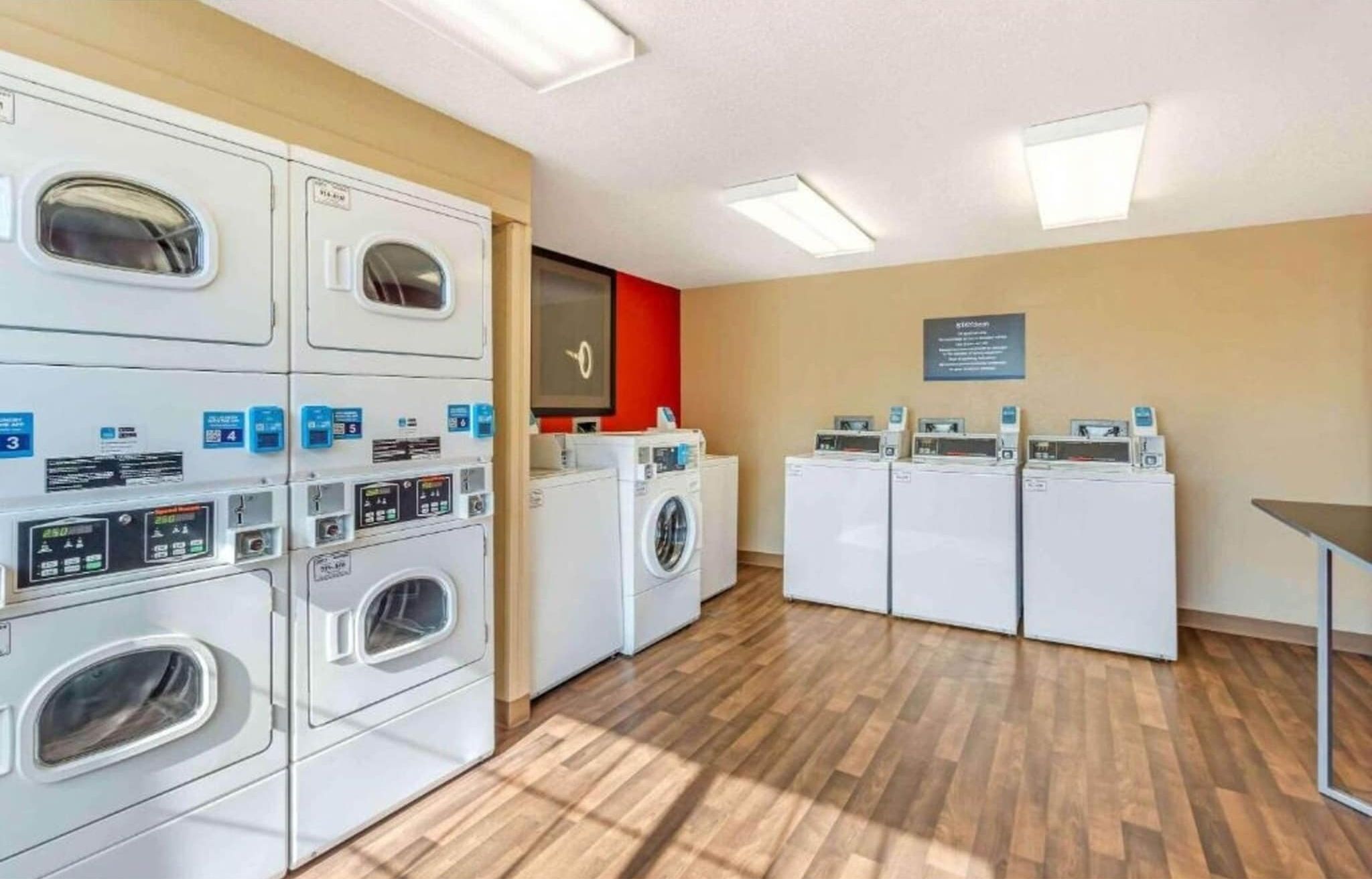 A laundry facility with multiple washing machines and dryers, wooden flooring, and a red accent wall.
