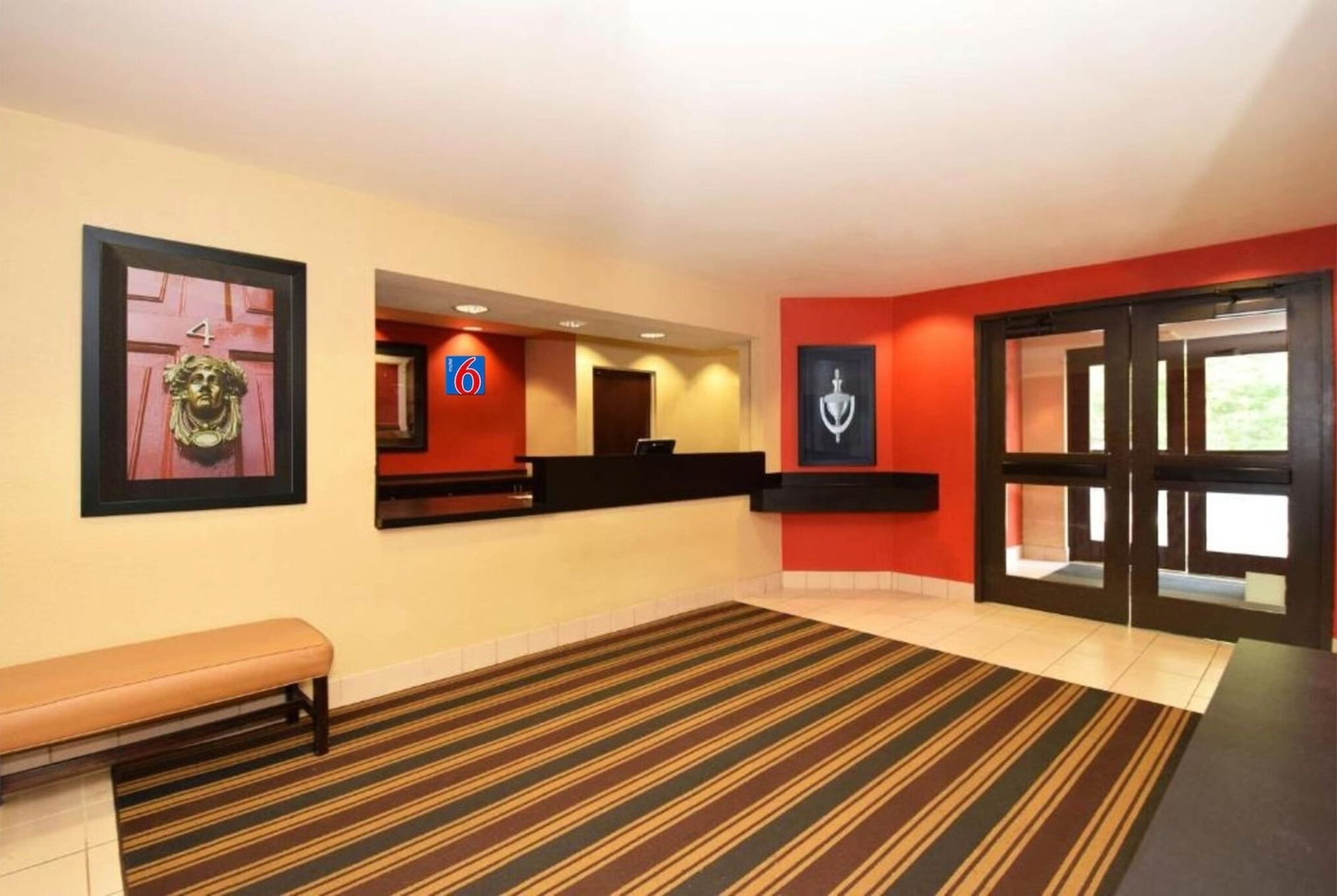 A hotel lobby with a reception desk, a bench, and a striped carpet.