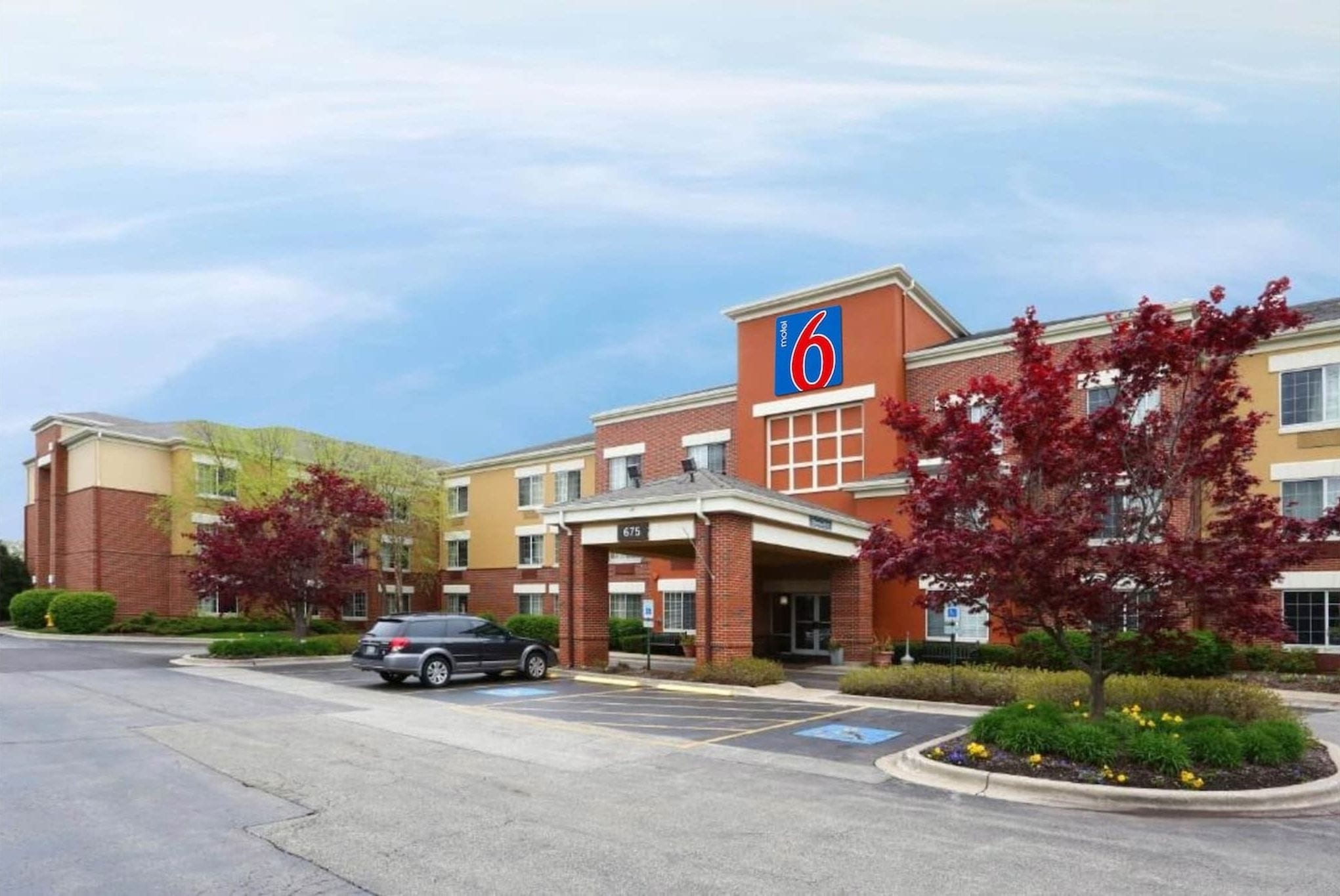 A motel with a prominent '6' sign, a parking lot, and a building with a brick facade.