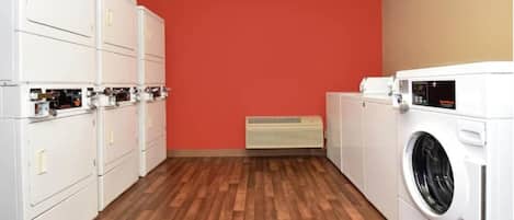 A laundry room with white appliances, a red wall, and a wooden floor.