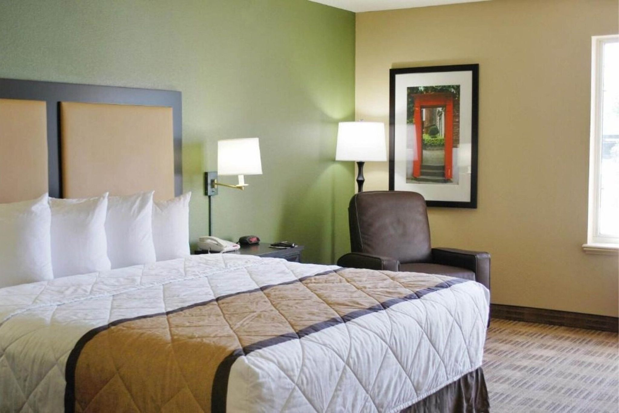 A hotel room with a large bed, a chair, a nightstand, and a wall-mounted lamp.