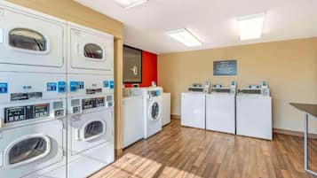 A laundry facility with multiple washing machines and dryers, wooden flooring, and a red accent wall.