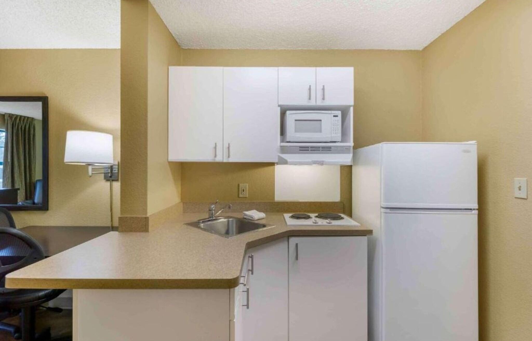 A compact hotel kitchen with white cabinets, a microwave, a stove, and a refrigerator.