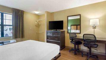A hotel room with a bed, a desk with a chair, a television, a mirror, and a window with curtains.