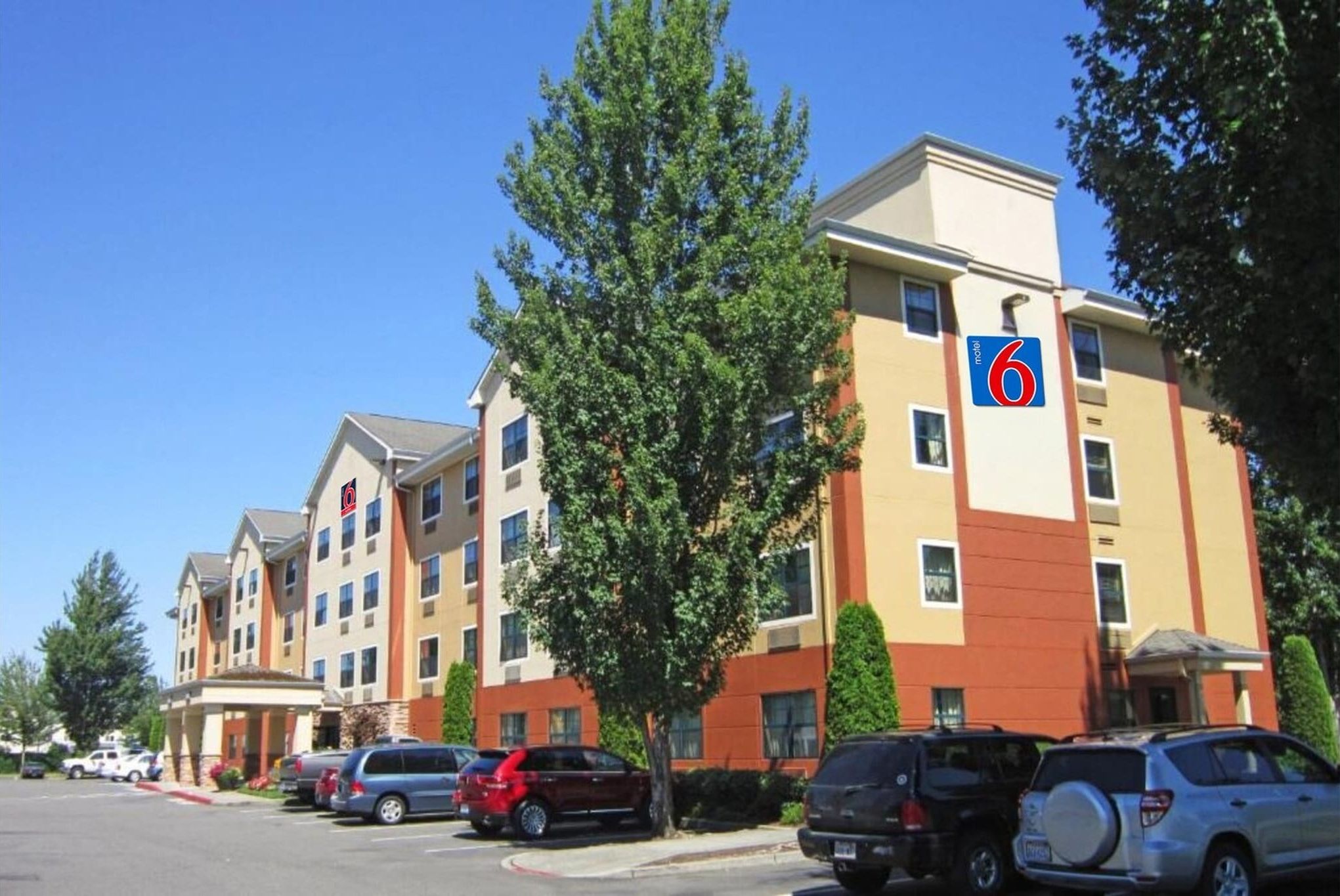 A hotel with multiple floors, a parking lot with several cars, and a clear blue sky.