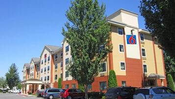 A hotel with multiple floors, a parking lot with several cars, and a clear blue sky.