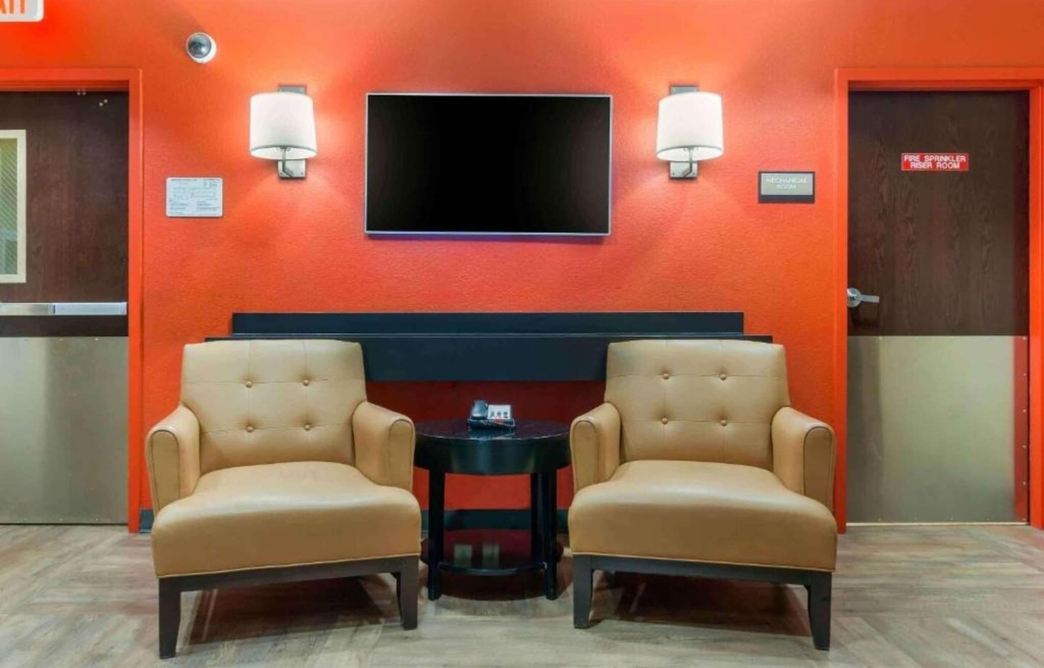 A room with two leather armchairs, a small table, a flat-screen TV, and a fire sprinkler room sign.