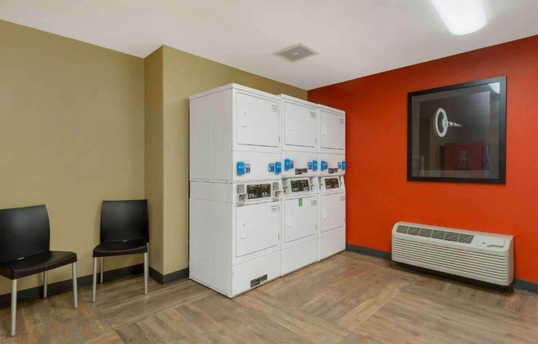 Een kamer met een ruime witte kastruimte, twee zwarte stoelen, een airconditioningsysteem en een lijst met een afbeelding aan de muur.