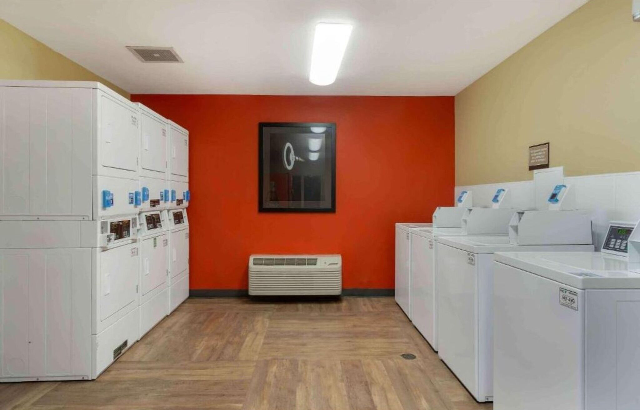 A laundry facility with stacked washers and dryers, a central air vent, and a framed picture on the wall.