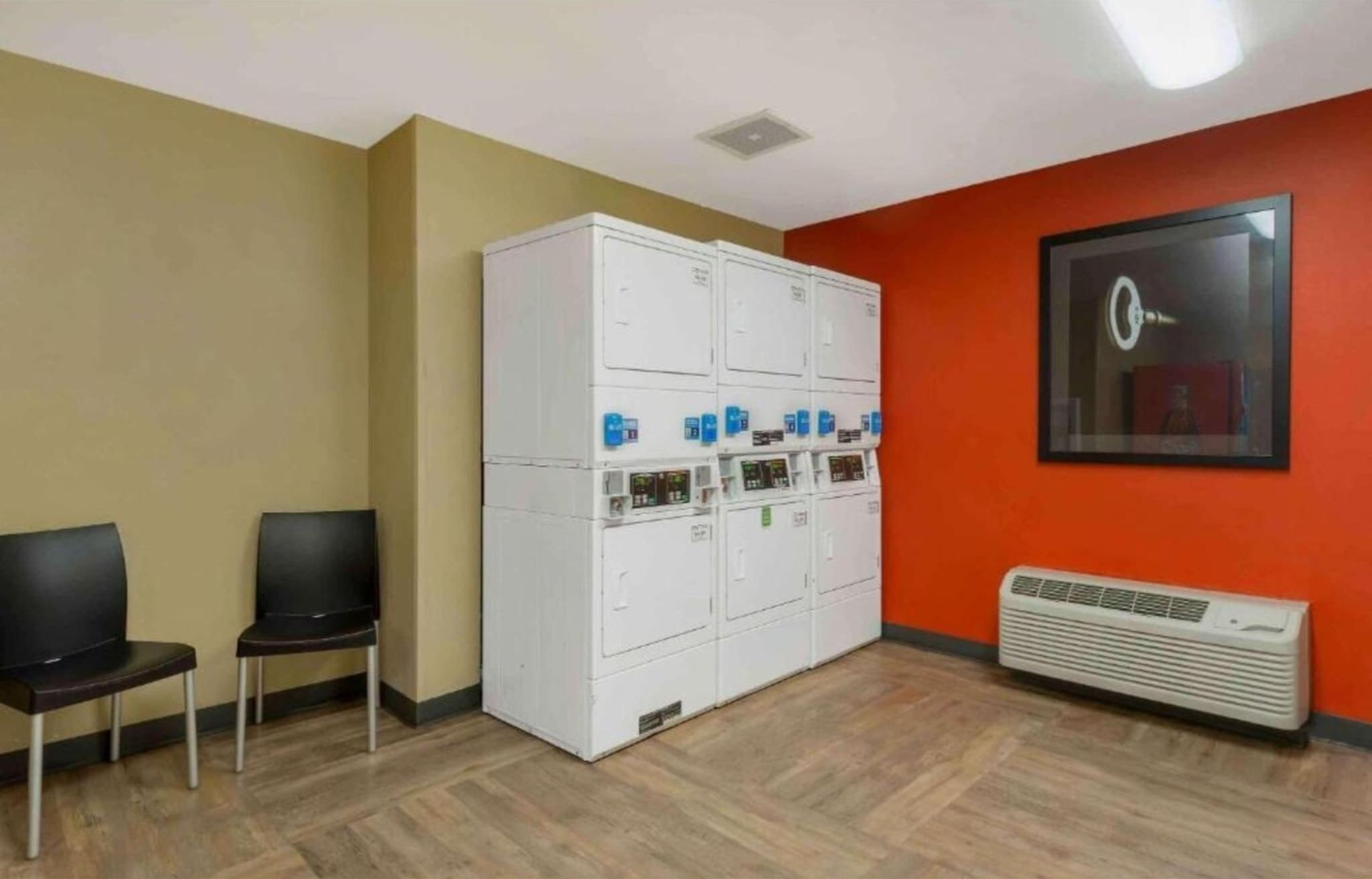 A room with a large white locker area, two black chairs, an air conditioning unit, and a framed picture on the wall.
