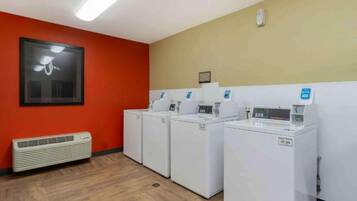 A laundry room with four white washing machines, a heater, and a framed picture on the wall.