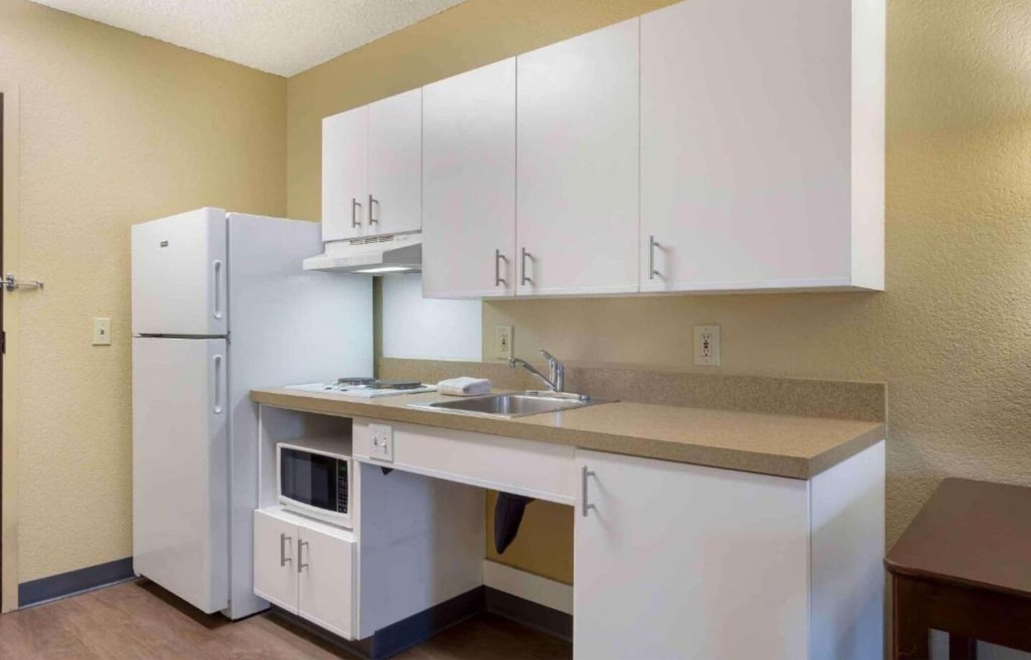 A compact kitchen with white cabinets, a built-in microwave, and a stainless steel sink.