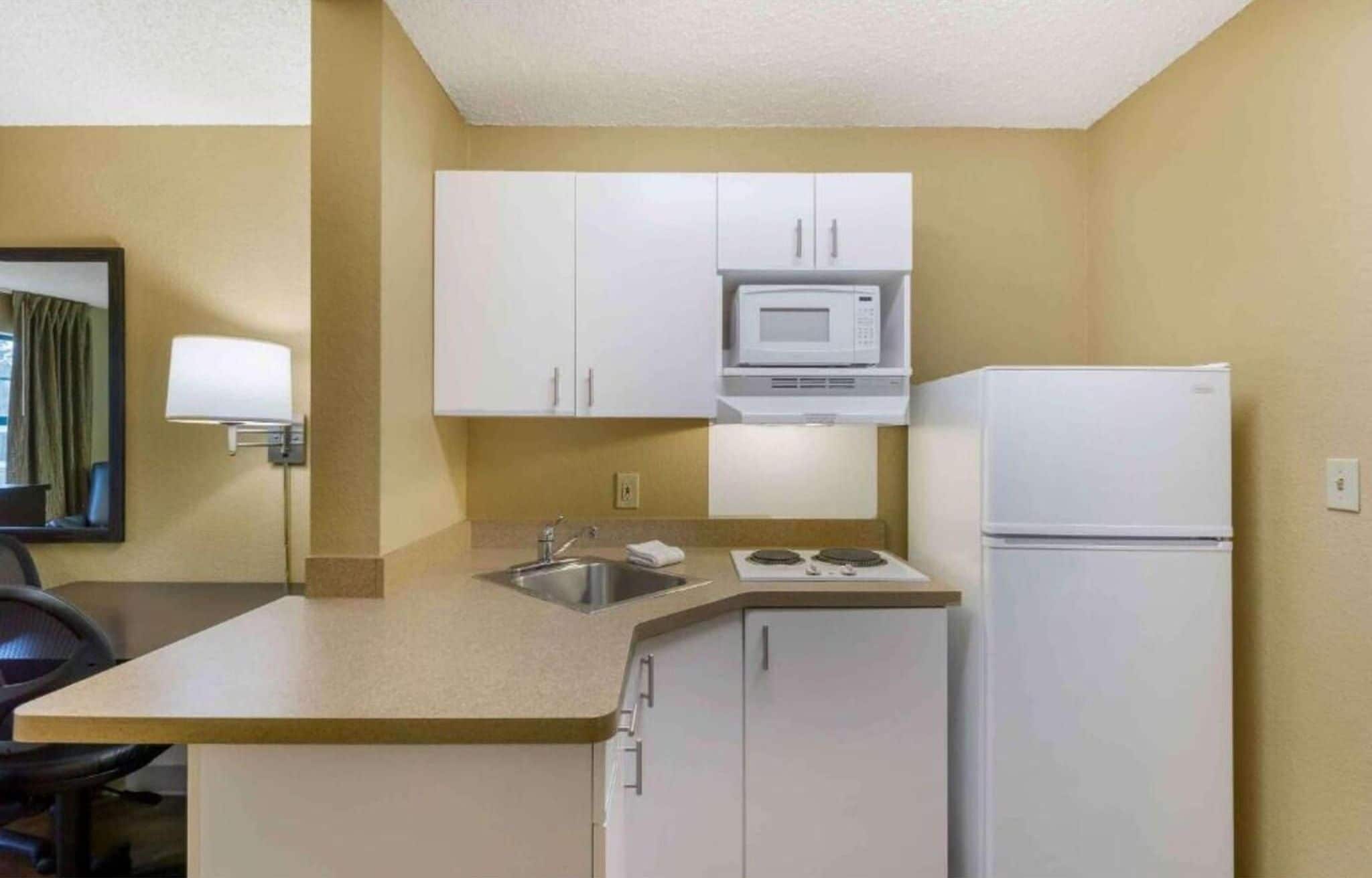 A compact hotel kitchen with white cabinets, a microwave, a stove, and a refrigerator.