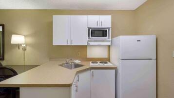 A compact kitchenette with a microwave, stove, and refrigerator, a sink, and a chair.