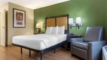 A hotel room with a bed, a chair, a nightstand, a lamp, and a wall-mounted light fixture.