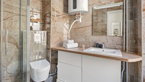 Ein modernes Badezimmer mit Marmor-Spritzschutz, einer Glasdusche, einem weißen Waschbecken und einer integrierten Toilette.