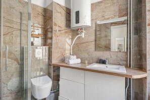 A modern bathroom with a marble backsplash, a glass shower enclosure, a white sink, and a built-in toilet. - Stay Near Sorbonne & Luxembourg Garden (Paris)