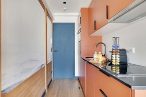 A compact kitchen with a blue door, a coffee machine, and a fruit bowl on the counter. - One-Bedroom Deluxe Apartment (Paris)