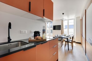 A modern kitchen with a black countertop, orange cabinets, and a dining area with a table and chairs. - One-Bedroom Deluxe Apartment (Paris)