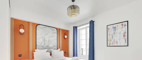 Une chambre moderne avec un grand lit, une œuvre d’art représentant une carte au mur, une fenêtre avec des rideaux et un luminaire suspendu.