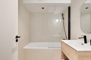 A modern bathroom with a bathtub, a shower, a sink, and a mirror. - One-Bedroom Deluxe Apartment (Paris)