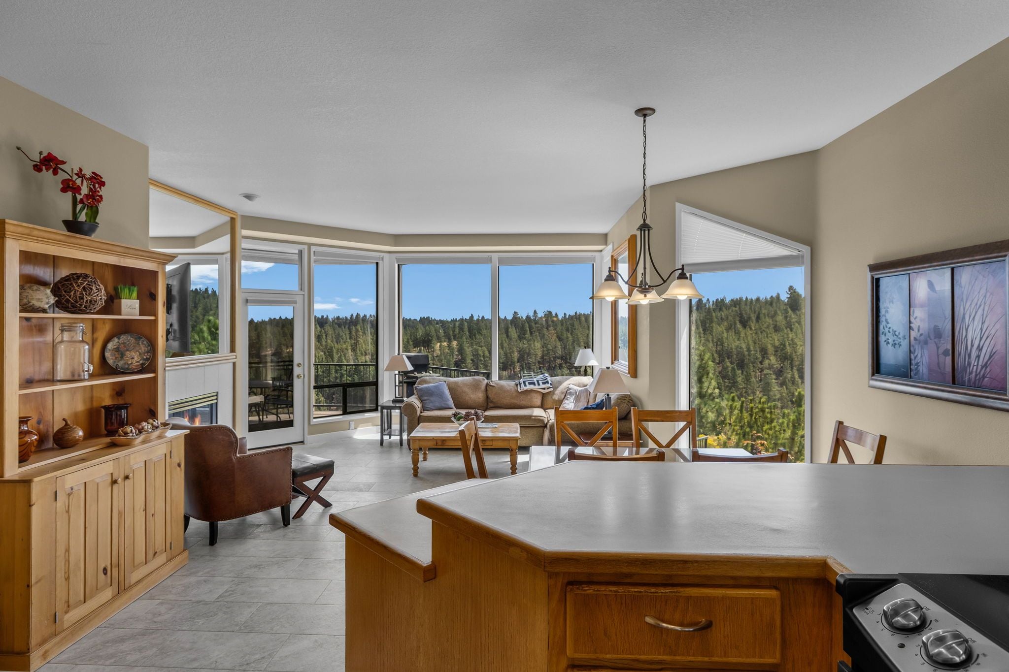 A spacious kitchen with a large island, wooden cabinetry, and a view of a forest through large windows.