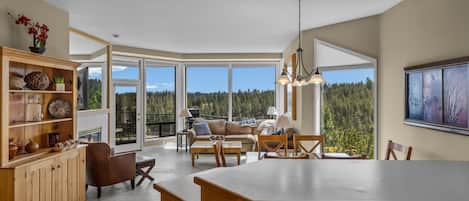 Una cocina amplia con una isla grande, armarios de madera y vistas a un bosque a través de ventanas panorámicas.