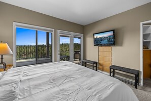 Una camera da letto con un letto grande, una TV fissata al muro, una porta vetrata scorrevole che dà su un balcone e un piccolo tavolo con una panca.