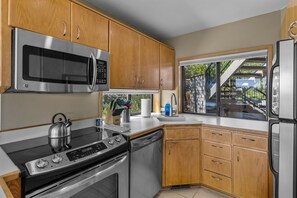 A modern kitchen with stainless steel appliances, wooden cabinets, and a window with a view of a staircase. - Mt Bachelor Village 321 | Hot Tub | Scenic Views (Bend)