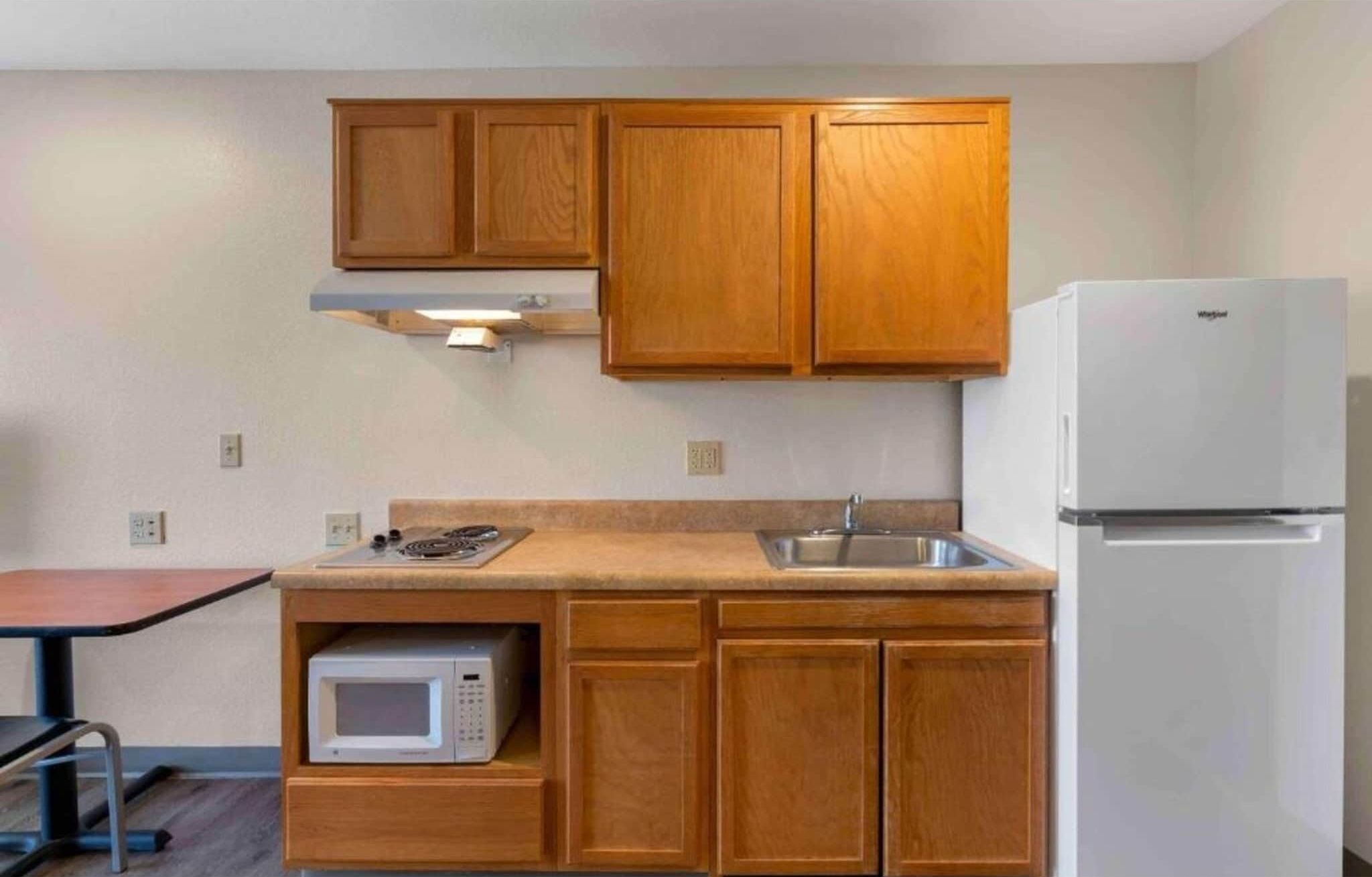 Eine kleine Küche mit Holzschränken, einer Mikrowelle, einem Spülbecken und einem weißen Kühlschrank.