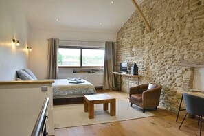 A room with a bed, a desk, a chair, a small table, and a stone wall. - Holiday home with 1 bedroom (SAINT-LATTIER)