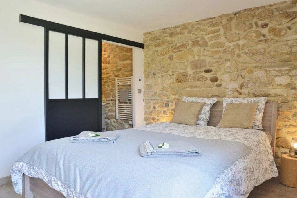 A bedroom with a stone wall, a bed with a floral bedspread, and a nightstand with a lamp.